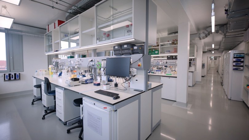 Modern ausgestattetes Labor mit zentralem Arbeitstisch und Deckenversorgung.