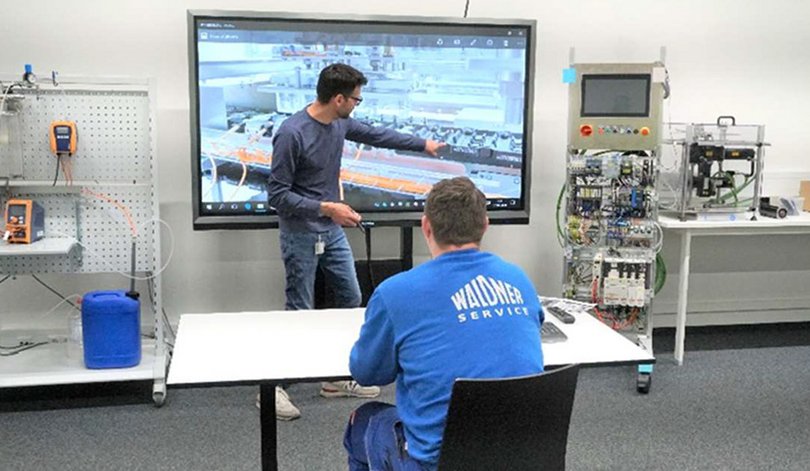 Service Mitarbeitender erhält Schulung vor großem Display mit Maschinenansicht.