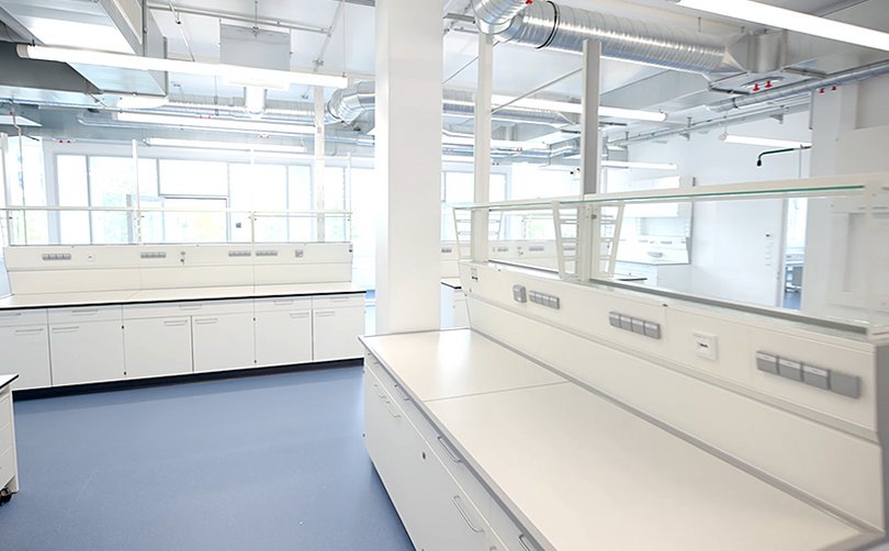 Heller Laborraum mit Arbeitsinseln und Lüftungsleitungen.