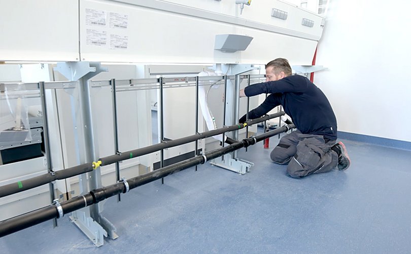 Monteur installiert Leitungen unter Labortisch.